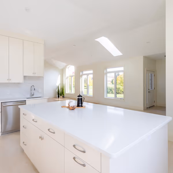 Modern kitchen with white cabinetry, large island with dark base, two wicker bar stools, and large windows with white shutters.