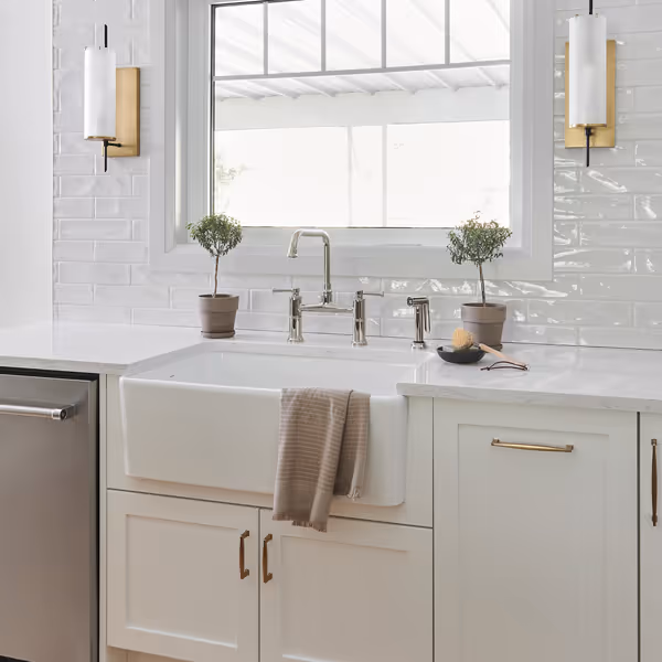 Modern kitchen sink with dual stainless steel basins and a tall curved chrome faucet under white shuttered window.