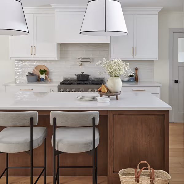 Modern kitchen with white cabinetry, large island with dark base, two wicker bar stools, and large windows with white shutters.
