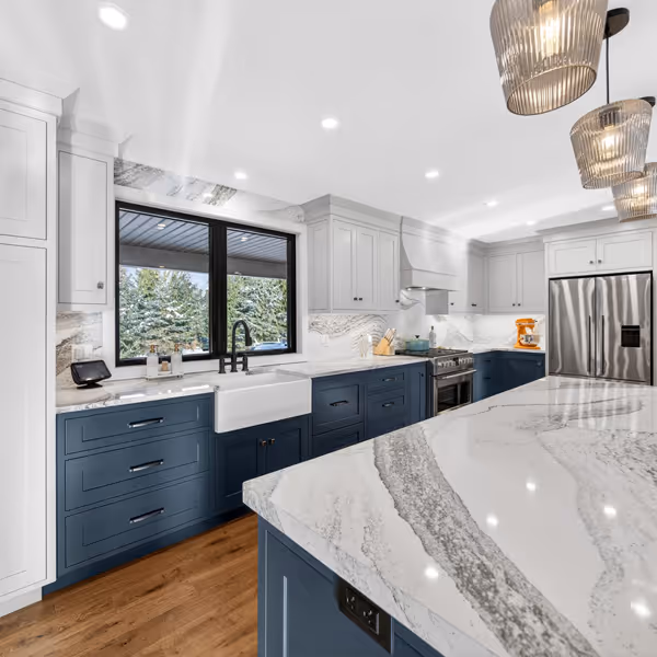 Modern kitchen sink with dual stainless steel basins and a tall curved chrome faucet under white shuttered window.