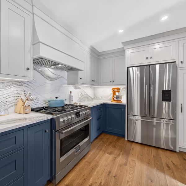 Modern kitchen with white cabinetry, large island with dark base, two wicker bar stools, and large windows with white shutters.