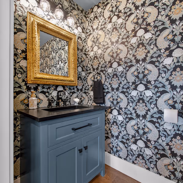 Cozy living room with cream sofa, patterned armchairs, wooden floor, and a decorated Christmas tree near a large window.