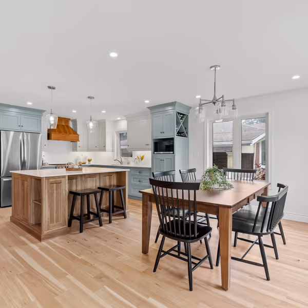 Cozy living room with cream sofa, patterned armchairs, wooden floor, and a decorated Christmas tree near a large window.
