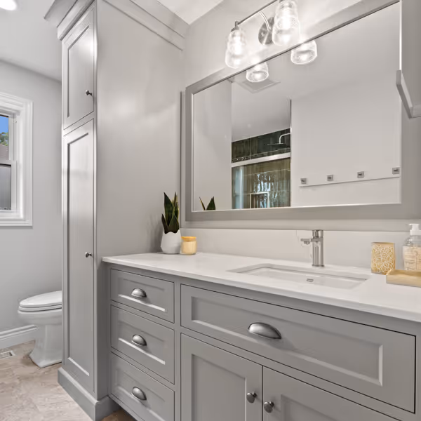 Cozy living room with a white fireplace decorated with greenery and red berries, a mounted TV above, a brown leather sofa on the left, and a beige patterned armchair on the right.