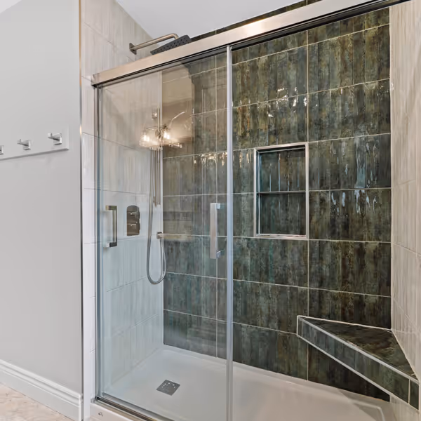 A bright modern bathroom with double vanity sinks, two rectangular mirrors, wall sconces, white cabinetry, and patterned tile floor.