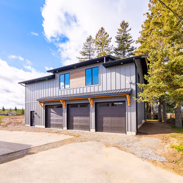 Modern white kitchen with stainless steel refrigerator, built-in oven and microwave, hardwood floor, and a woven chair at a white countertop.