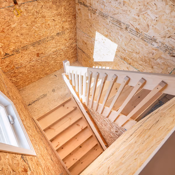 Modern kitchen shelving with wooden floating shelves displaying glassware, a small framed photo, bowls, a decanter, and flowers, above a countertop and wooden cabinets, with a dining table and chairs in the foreground.