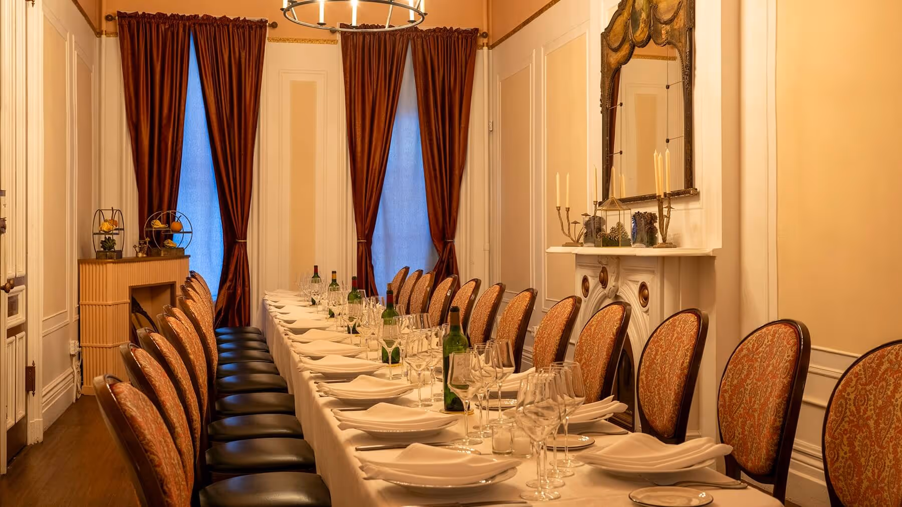 Elegant dining room with a long table set for dinner with white tablecloth, plates, glasses, wine bottles, and cushioned chairs.