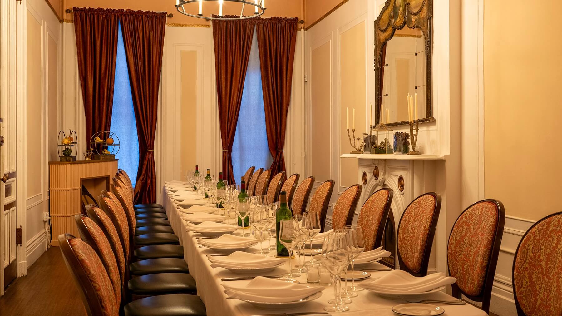 Elegant dining room with a long table set for dinner with white tablecloth, plates, glasses, wine bottles, and cushioned chairs.