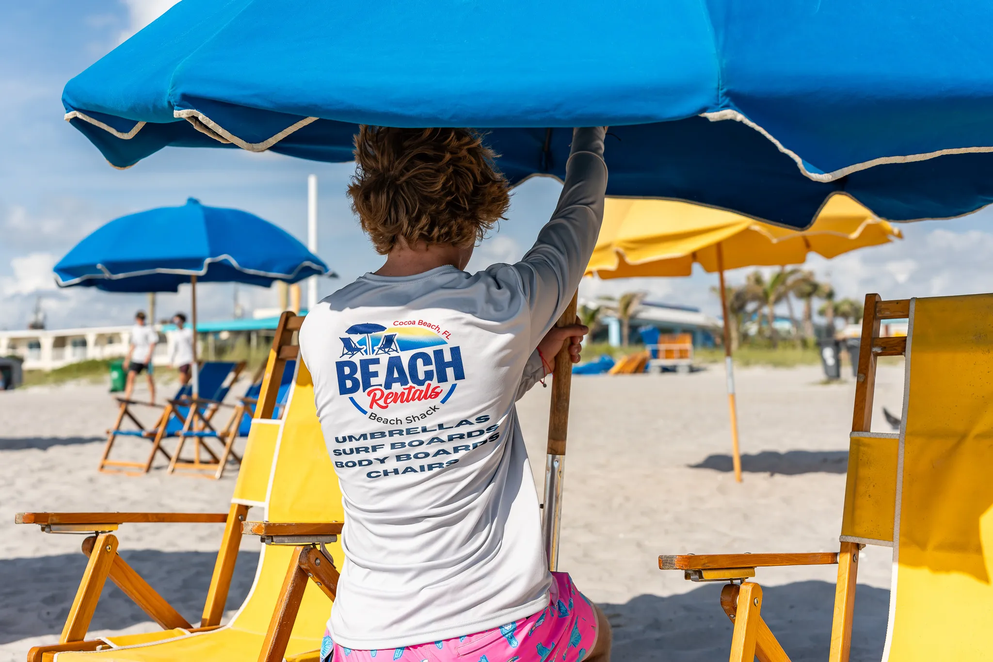 Commercial-grade large blue umbrellas and yellow beach chairs on Beach Shack Beach Rental's exclusive Cocoa Beach FL shoreline.