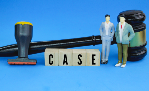 A judge's gavel, a rubber stamp, and miniature figures stand beside blocks spelling "CASE," symbolizing legal representation and the court process in a criminal case.