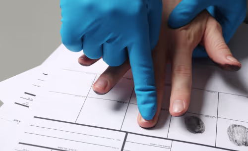 A gloved law enforcement officer takes a person's fingerprints on an official fingerprint card during the booking process following an arrest.
