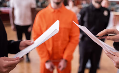 A person in jail attire stands in handcuffs while legal documents are reviewed, representing the criminal court process following a DUI arrest.