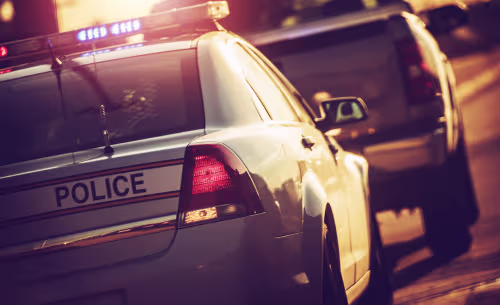 A police vehicle with flashing emergency lights follows a car at night, depicting a traffic stop related to a DUI investigation.