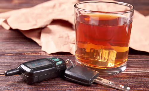 A glass of whiskey sits beside a car key and a portable breathalyzer, symbolizing alcohol consumption and impaired driving.