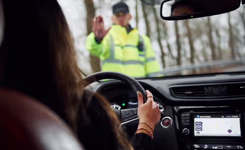 A police officer in a high-visibility jacket signals for a driver to pull over at a roadside DUI checkpoint or traffic stop.