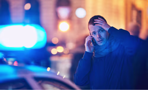 A stressed driver makes a phone call next to flashing police lights, illustrating the decision to contact a DUI lawyer during or immediately following a traffic stop.