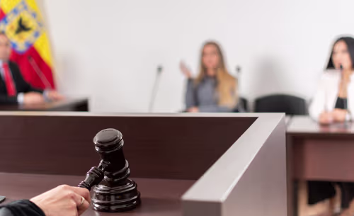 A judge holds a wooden gavel on the bench during a formal DUI court proceeding with attorneys and a witness visible in the background.
