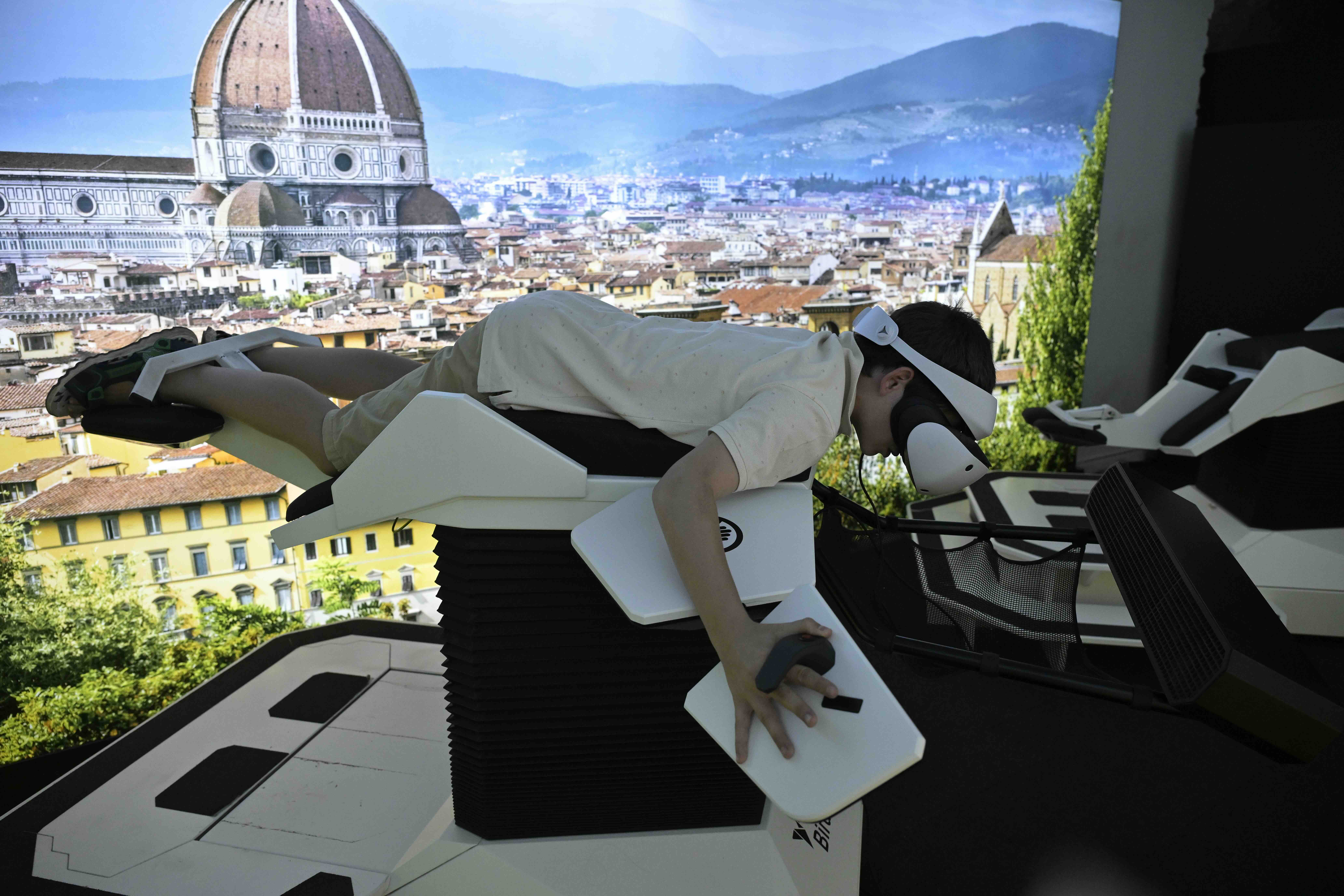 Child lying on a VR flight simulator wearing an Pico VR headset and holding flight controls.