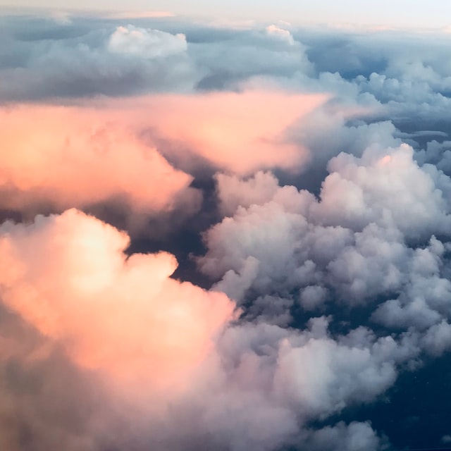 Fluffy clouds lit by soft pink and orange light at sunrise or sunset from above.