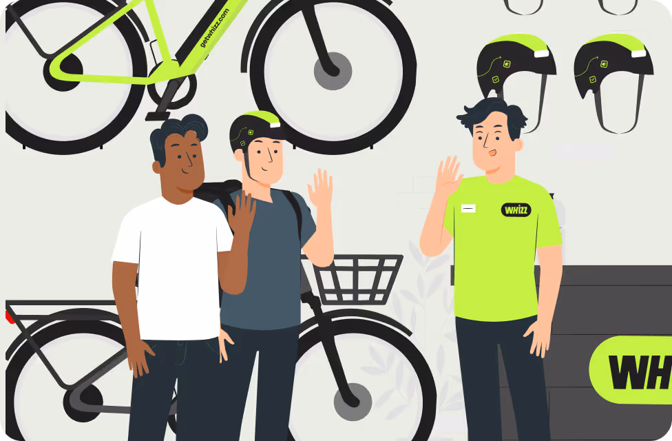 Three people waving in a bike rental shop with green and black bikes and helmets.