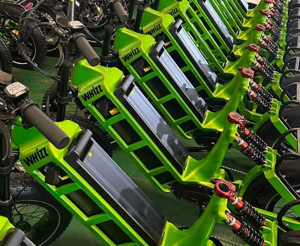 Row of bright green WHIZZ electric bikes lined up indoors with visible handlebars and suspension.