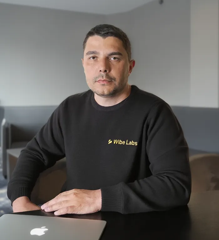 Man wearing a black Wibe Labs sweater sitting at a table with a closed Apple laptop.