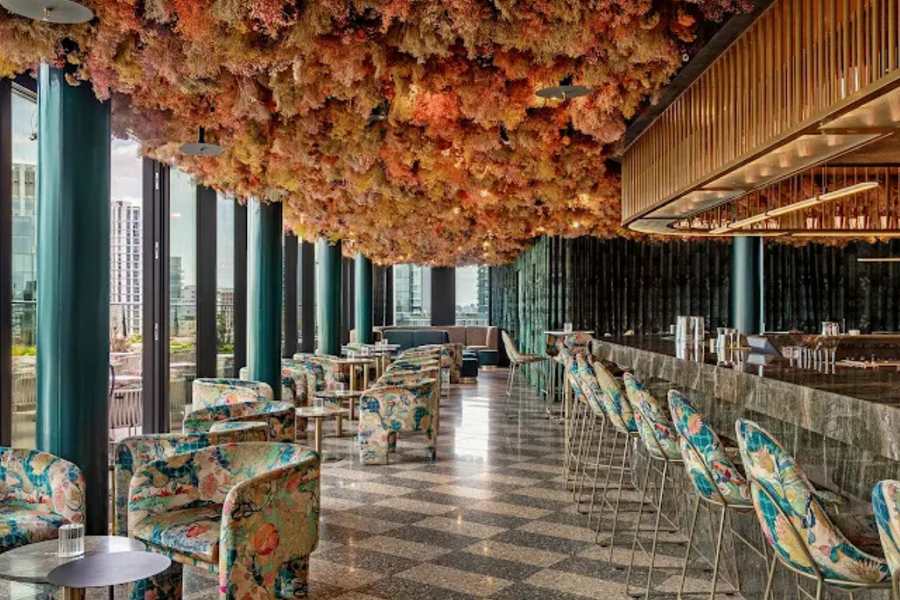 A stylish lounge area with floral print chairs, a stone bar, and a ceiling covered in colourful dried flowers.