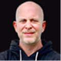 Smiling bald man wearing a black hoodie against a black background.