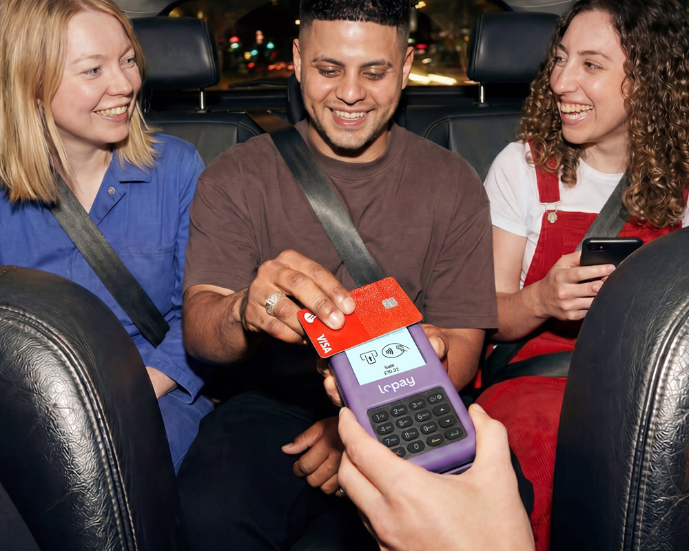 Man in backseat using red Visa card to pay with a purple Lopay card reader, two women smiling nearby.