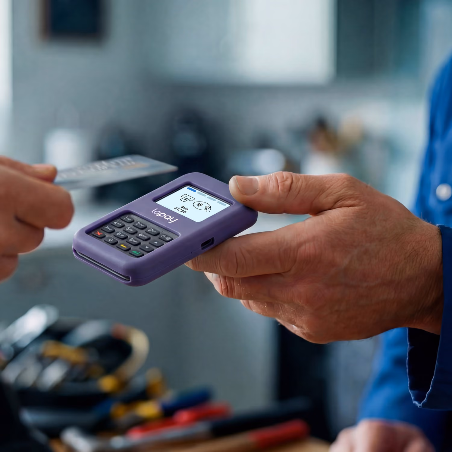 Close-up of a purple lopay wisepad card reader held by a man, with another hand tapping a contactless card.