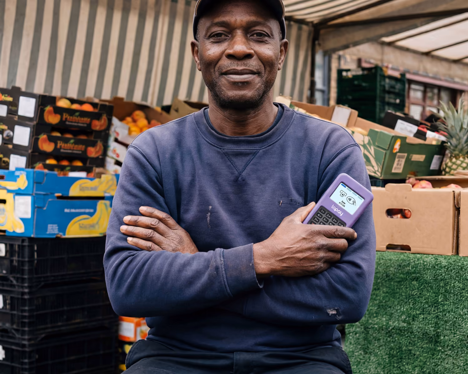 Man holding a WisePad 3 payment terminal in front of a fruit and vegetable market stall.