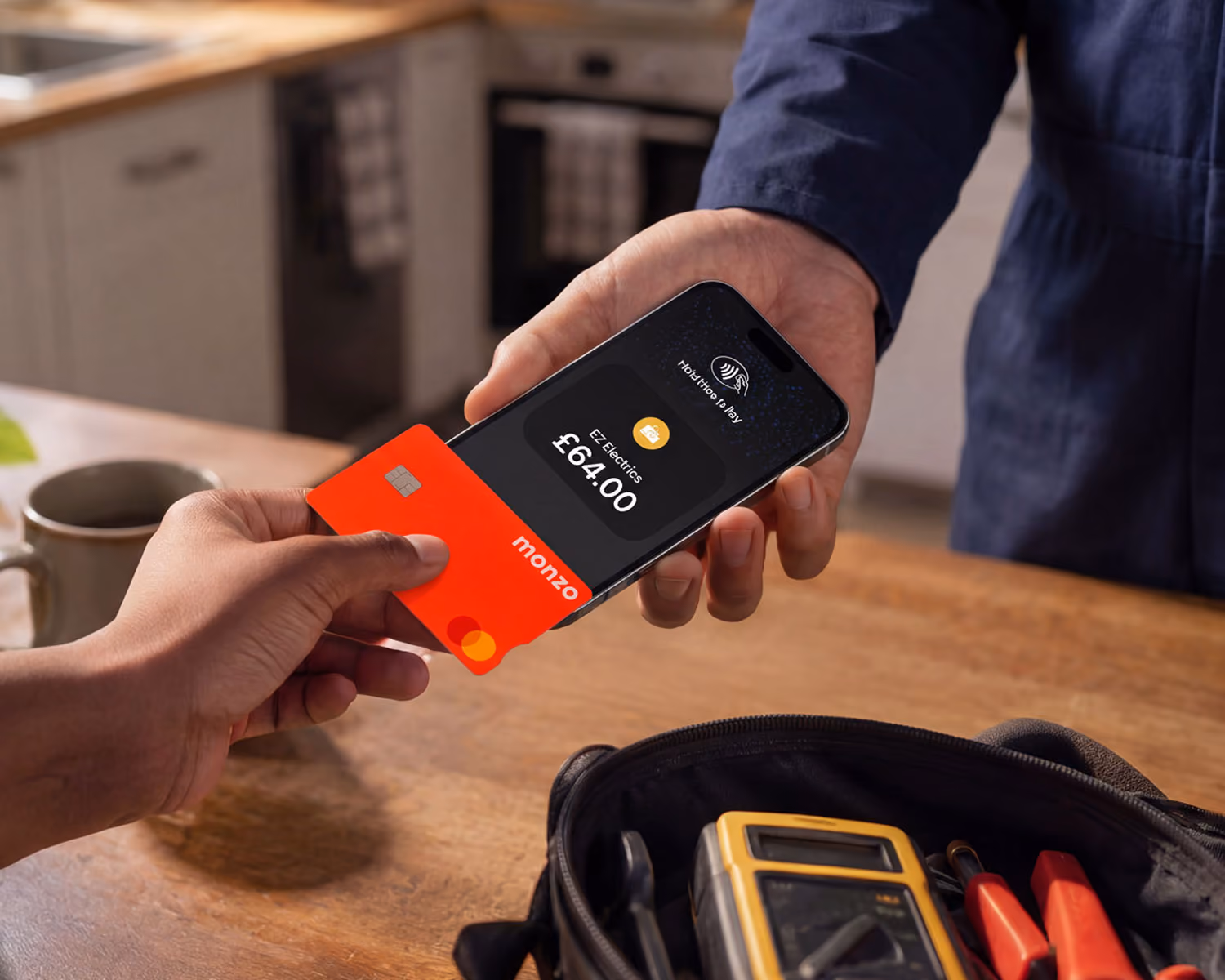 Person making a £64 contactless payment to a plumber with an orange debit card on a phone in a kitchen.