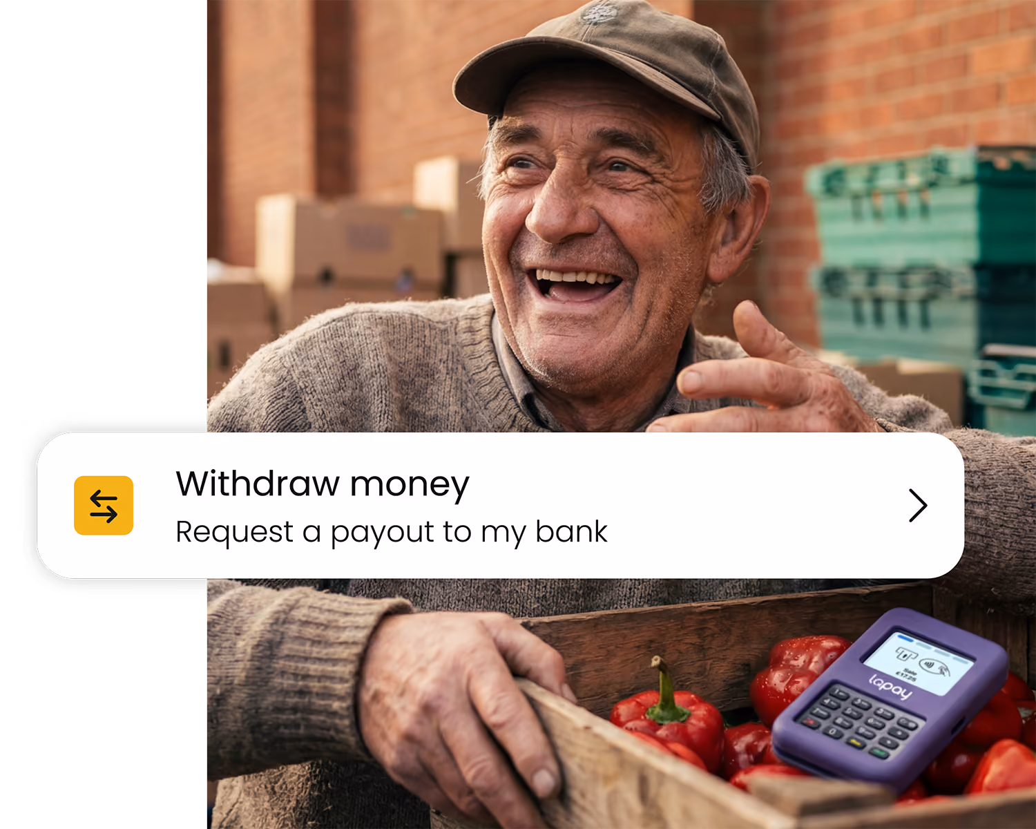 Smiling elderly man holding a crate of red peppers and a purple payment terminal outdoors.