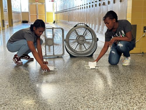 Two students with paper model wind-powered cars.