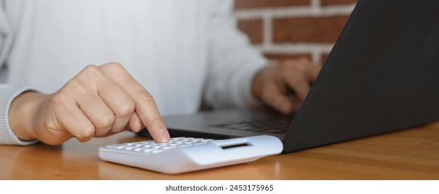 A person using a calculator beside a laptop at a desk