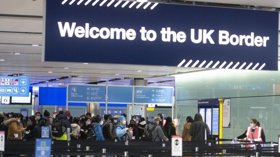 Travellers queuing beneath a 'Welcome to the UK Border' sign at an airport