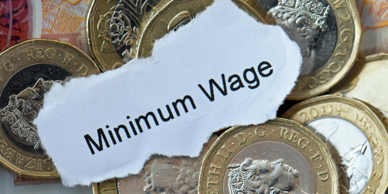 A note reading 'Minimum Wage' resting on British pound coins