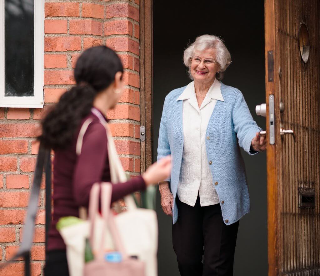 A Home Instead care worker welcomed at an older woman's front door