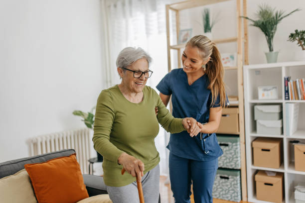 A care worker supporting an older woman with a walking stick at home