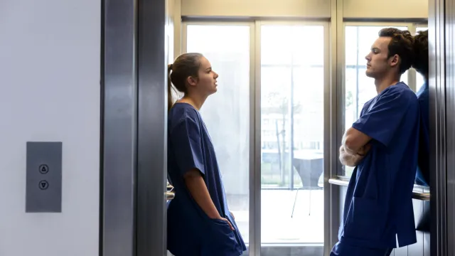 Two healthcare workers in scrubs talking by a lift