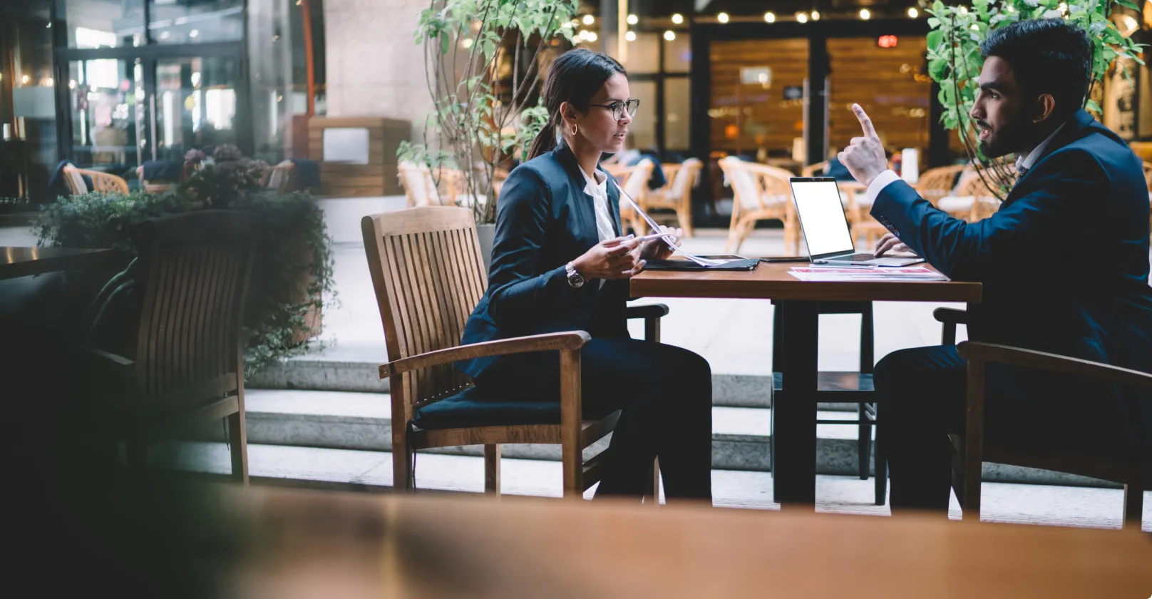 man and woman talking at a table outside with greenery in the background