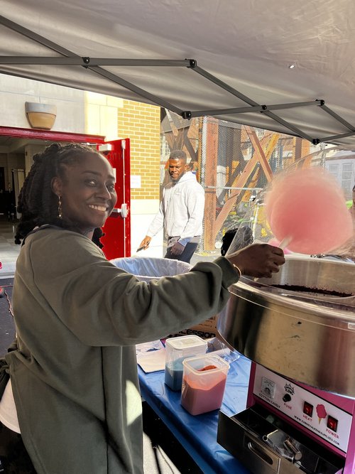 Smiling volunteer spinning pink cotton candy at school carnival booth
