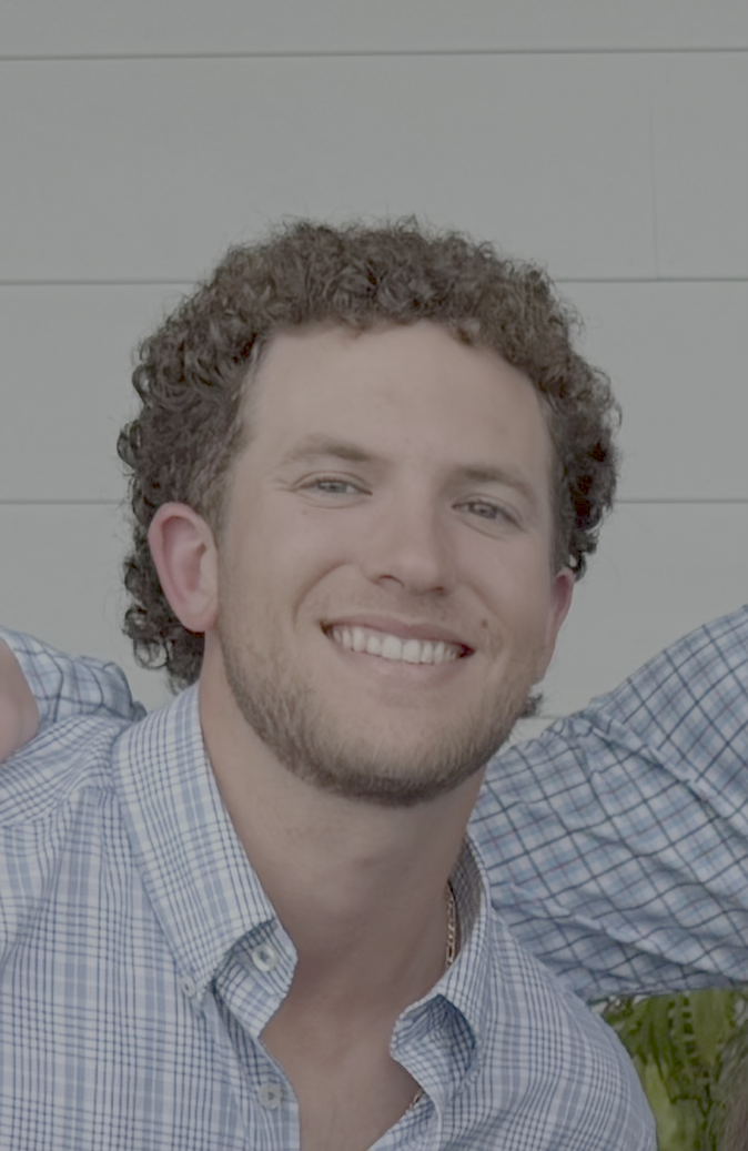 Smiling man with curly hair wearing a blue checkered shirt.