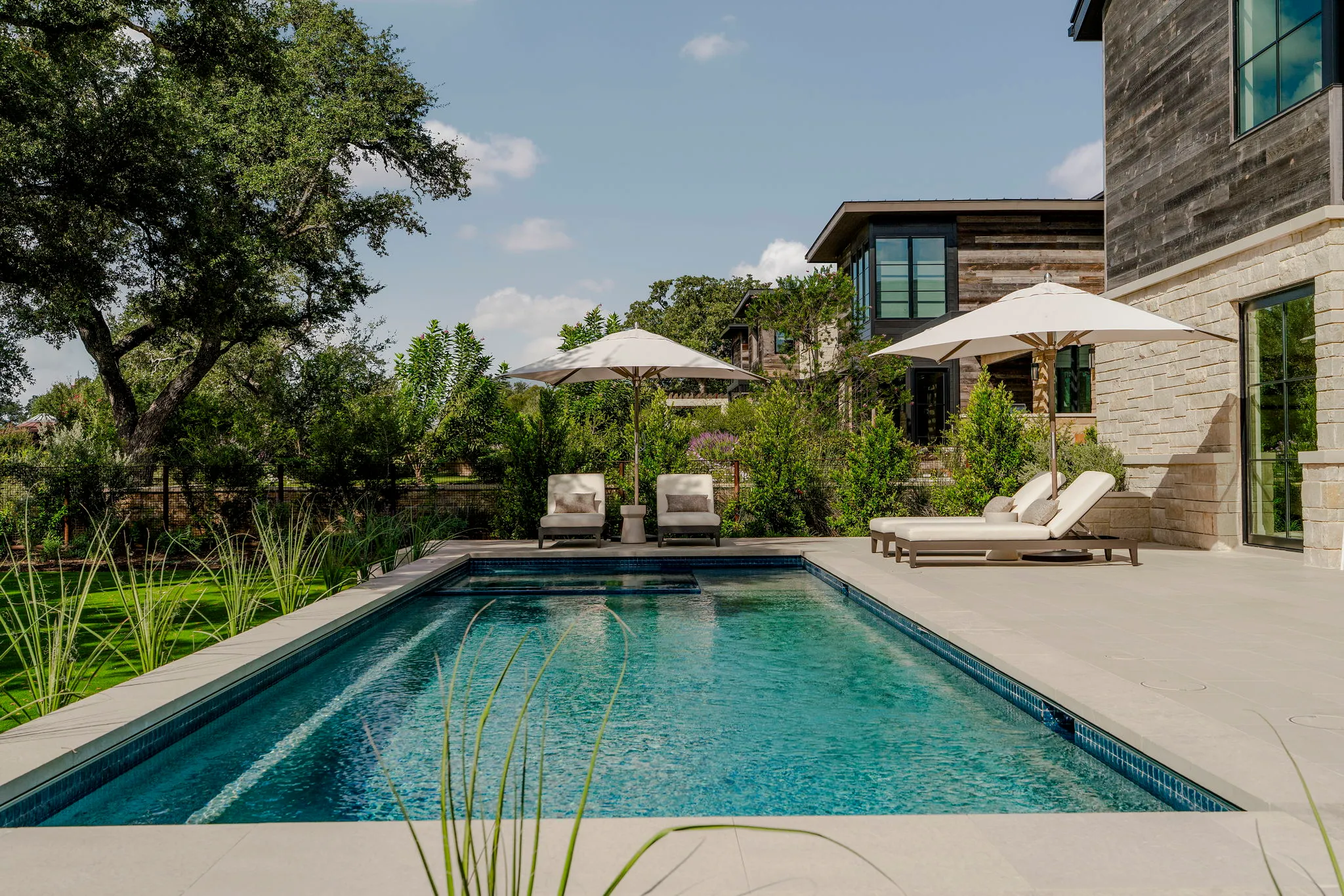 Rectangular pool with lounge chairs, framed by trees and the rear of the home