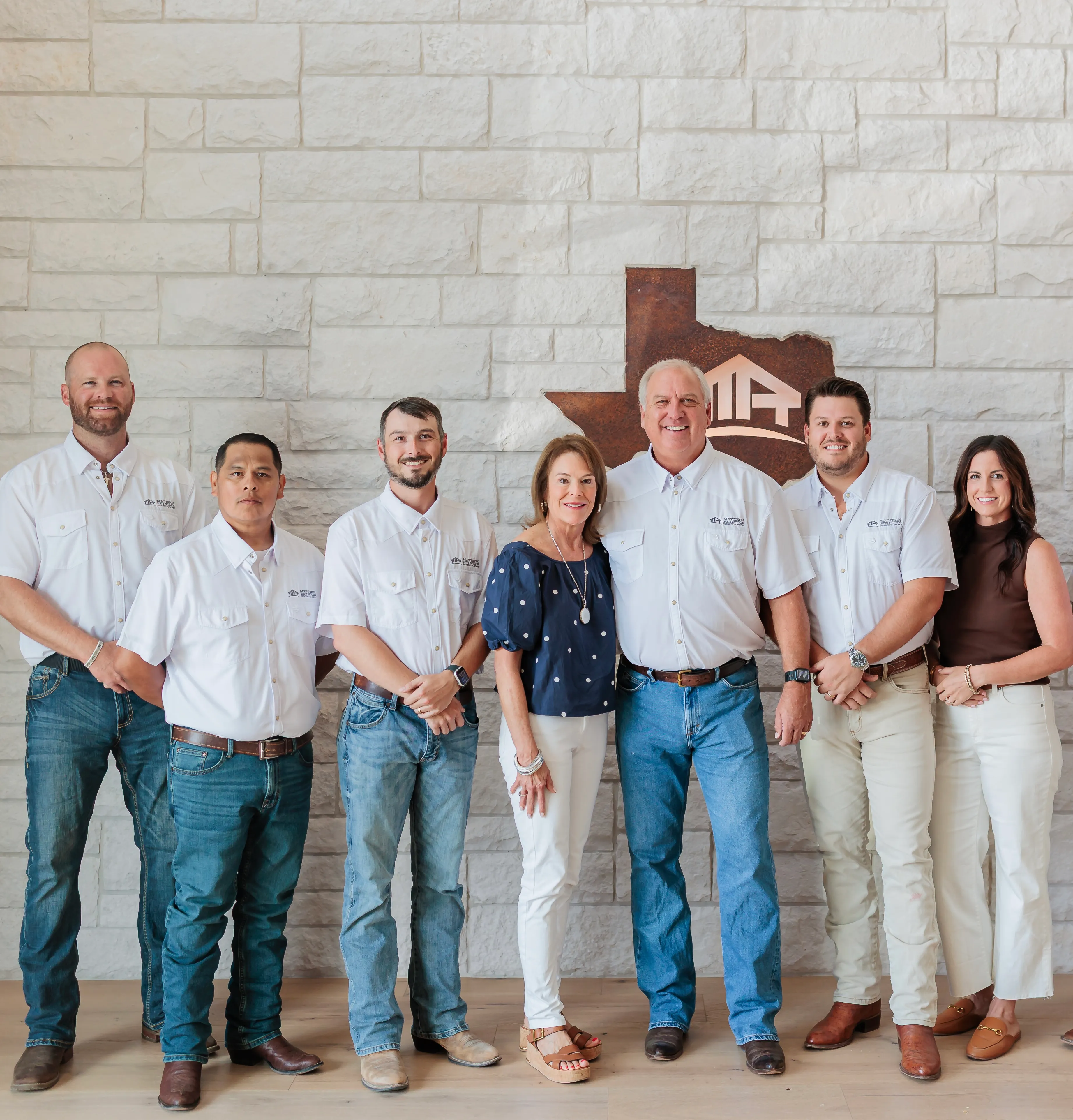 The MRRW Homes team in white work shirts in front of a stone wall with the Texas logo sign