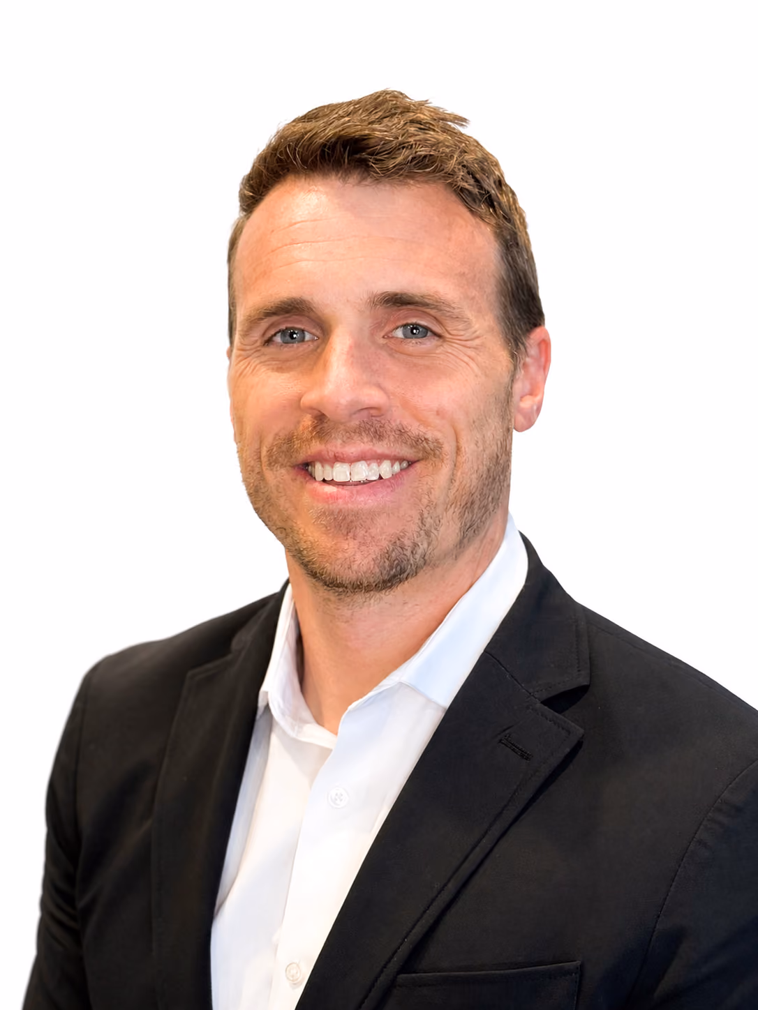 Smiling man with light brown hair, a short beard, wearing a black blazer over a white button-up shirt, against a white background.