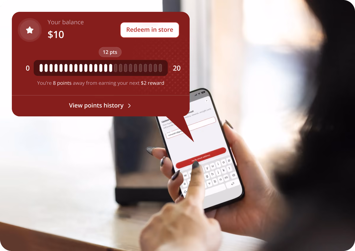 Person using a smartphone app with a loyalty balance of $10 displayed, showing 12 points earned out of 20, and a message indicating 8 points needed for a $2 reward, with options to redeem in store and view points history.