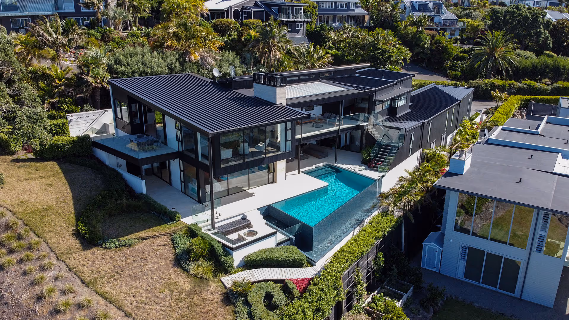 Aerial view of a modern two-story house with a swimming pool, glass railings, and surrounding lush greenery.