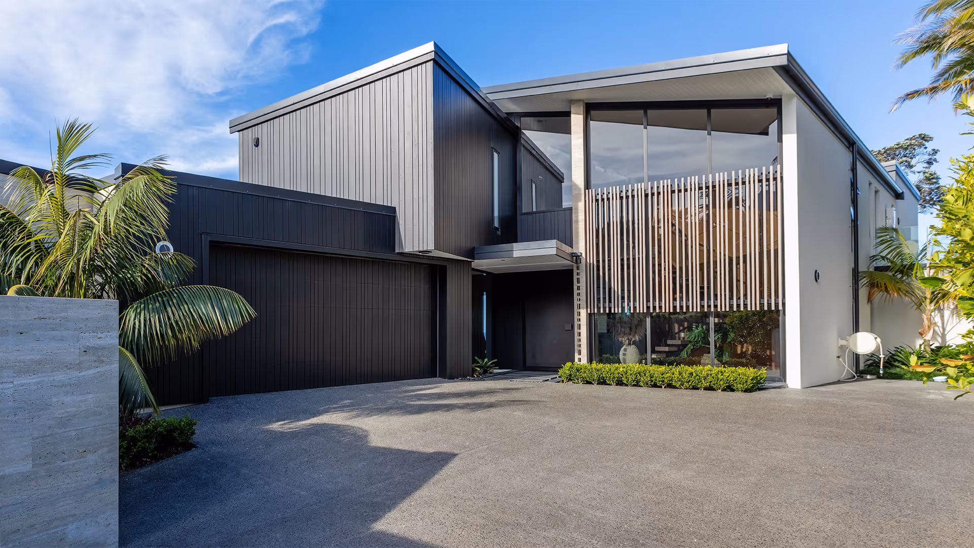 Modern two-story house with black vertical siding, large windows with wooden slats, and a spacious driveway.